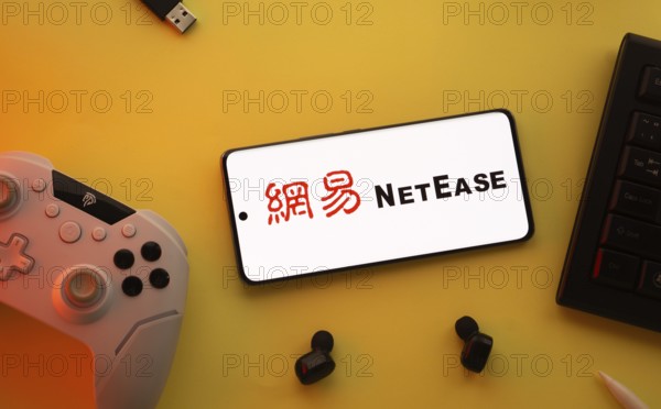 Dhaka, Bangladesh- 23 March 2025: NetEase logo displayed on a smartphone surrounded by gaming accessories in an yellow light