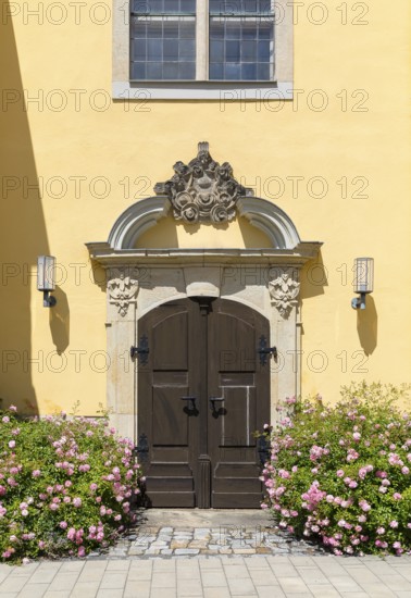 Side portal with sandstone decorations and blooming rose bushes at the town church of St. Nicolai in Pulsnitz, Saxony, Germany