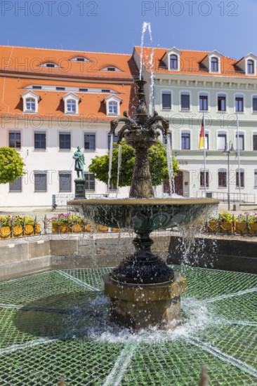 Sandstone market fountain on the medieval market square, in the background the monument to the sculptor Ernst Rietschel, Pulsnitz, Saxony, Germany