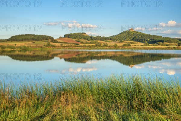 Wachsenburg Castle is reflected in the still water of a lake under a blue sky with cumulus clouds, shore with grass, castle of the castle ensemble Drei Gleichen, Thüringer Burgenland, Mühlberg, Thuringia, Germany