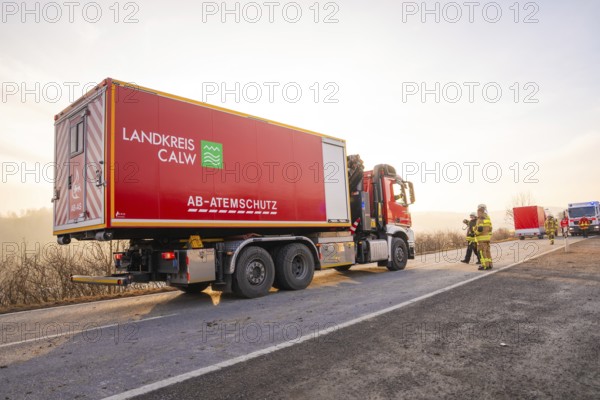 A large red fire truck is parked on a landscape road in the morning light, firefighters next to it, fire department exercise on the Hermann Hesse Railway, Ostelsheim, Calw district, Germany