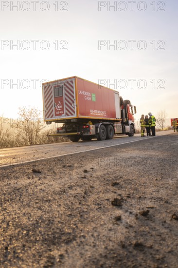 A fire truck is parked on a street at sunrise with firefighters nearby, fire department practice at the Hermann Hesse Railway, Ostelsheim, Calw district, Germany