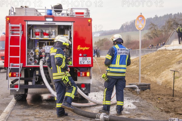 Firefighters are standing on a street near a fire truck. They are preparing hoses for use, fire brigade exercise at the Hermann Hesse Railway, Ostelsheim, Calw district, Germany