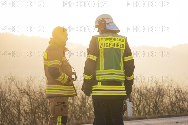 Two firefighters talking at sunset wearing safety vests on a street, fire department exercise on the Hermann Hesse railway, Ostelsheim, Germany