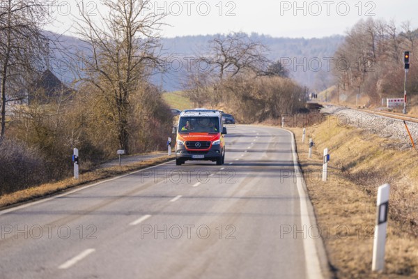 An ambulance is driving on a rural road, trees and railroad tracks in the background, fire department exercise on the Hermann Hesse Railway, Ostelsheim, Germany