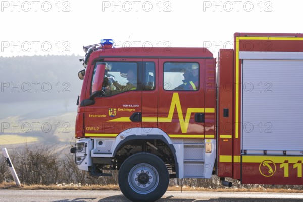 Side view of a red emergency vehicle on a wintry country road, fire department exercise on the Hermann Hesse railway, Ostelsheim, Germany