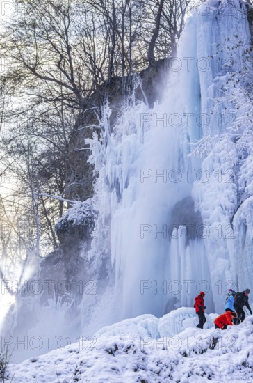 Spectators climb on the Urach waterfall full of bizarre ice formations, frozen at low winter temperatures, Bad Urach, Swabian Alb, Baden-Württemberg, Germany