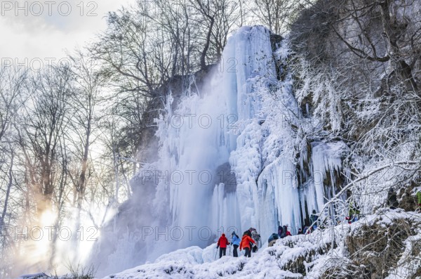 Spectators climb on the Urach waterfall full of bizarre ice formations, frozen at low winter temperatures, Bad Urach, Swabian Alb, Baden-Württemberg, Germany