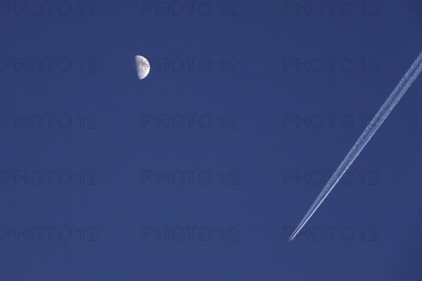 Airplane with contrails and moon in the evening sky, Germany