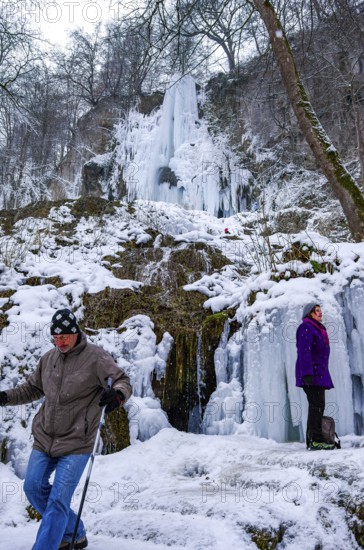Hikers climb on the Urach waterfall full of bizarre ice formations, frozen at low winter temperatures, Bad Urach, Swabian Alb, Baden-Württemberg, Germany, for editorial use only
