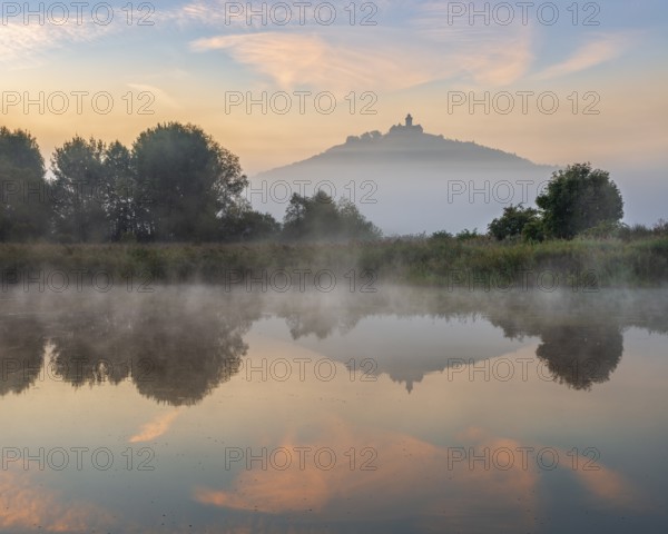 Wachsenburg Castle is reflected in the still water of a lake at sunrise, fog rises, castle of the castle ensemble Drei Gleichen, Thuringian Burgenland, Mühlberg, Thuringia, Germany