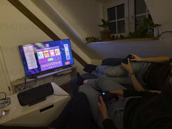 Friends sitting on the couch playing a video game on a TV with Steam Deck, video game Vampire Survivors, Munich, Bavaria, Germany