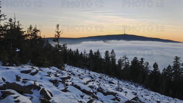 Landscape with snow-covered ground, trees and a mountain in the evening light, thick fog over the valley, Fichtelgebirge