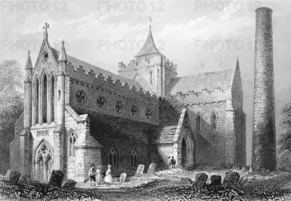 St Canice's Cathedral, County and City of Kilkenny, Ireland, 13th century catholic cathedral, 9th century round tower, medieval, gothic, cemetery, old tombstones, path, people, square church tower, landmark, steel engraving, 19th century, historical illustration from 1845