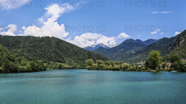 Turquoise blue lake surrounded by wooded mountains and bright blue sky, Slovenia