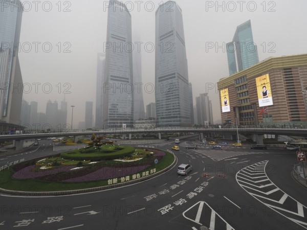 City scene with roundabout and skyscrapers in fog under grey sky, Pudong, Shanghai, China