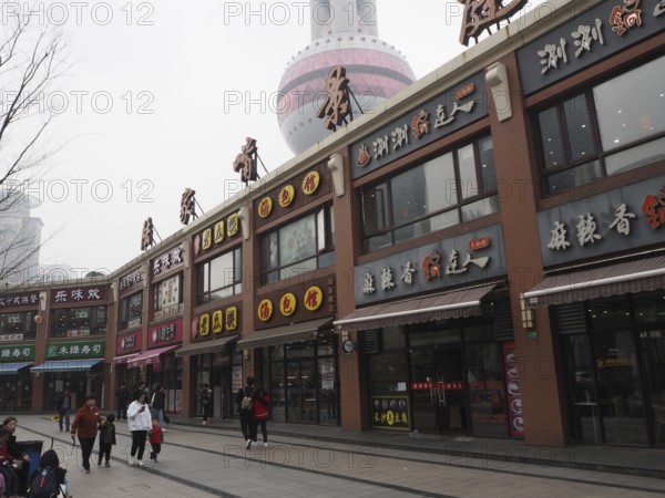 Commercial street with people and view of the TV tower on a cloudy day, Pudong, Shanghai, China