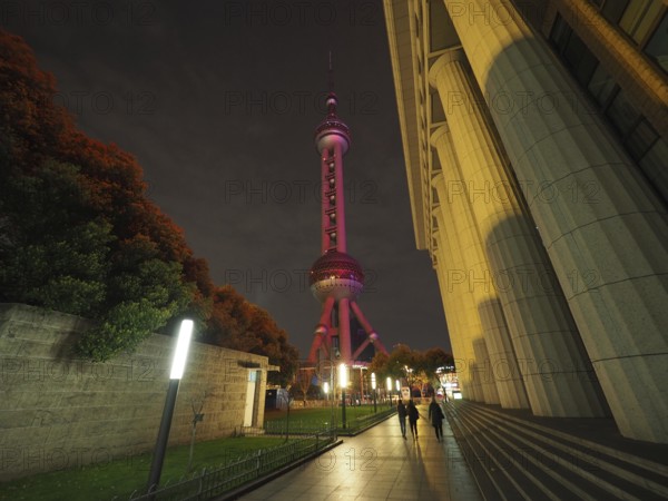 Illuminated television tower, Oriental Pearl Tower, in a nighttime street scene with people passing by, Shanghai, China