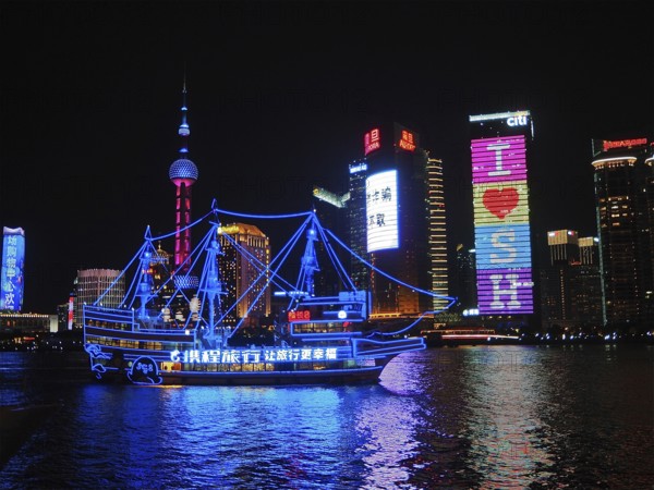 Illuminated skyline and river with an illuminated ship at night, Shanghai, China