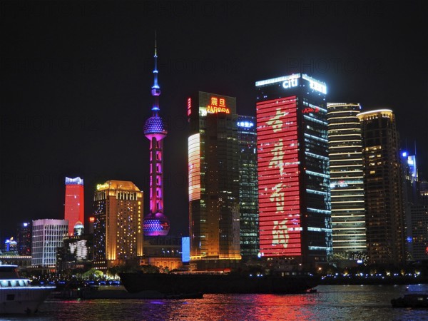 Illuminated skyscrapers and neon signs at night on a riverbank, Shanghai, China