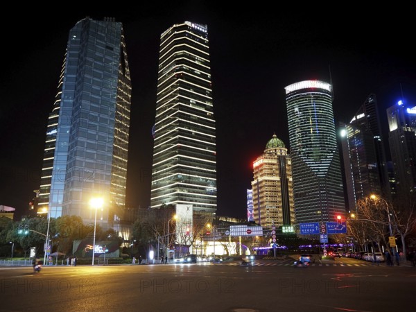 Illuminated skyscrapers in a modern city at night, with empty, well-lit street in the foreground, Shanghai, China
