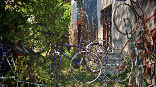 Colourful bicycles stacked on top of each other next to an art-painted wall surrounded by plants, Ljubljana, Slovenia