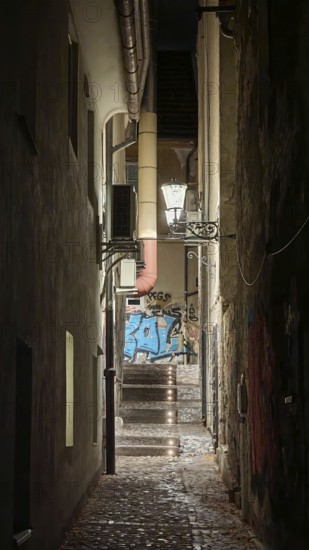 Narrow, illuminated alley at night with stairs lined with graffiti and old architecture, Ljubljana, Slovenia