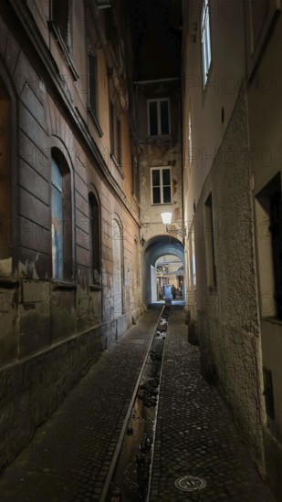 Dark, narrow alley at night with cobblestones and dim lantern light, urban atmosphere, Ljubljana, Slovenia