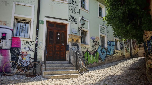 A paved street with ornate graffiti on walls and two bikes in front of a historic building, Ljubljana, Slovenia