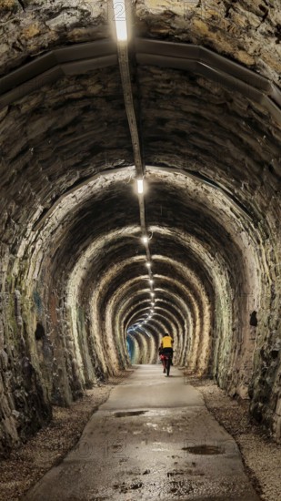 An illuminated tunnel with stone walls and a cyclist in the distance, Slovenia