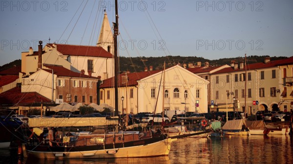 A harbor with sailboats and historic buildings in the warm evening sun, Izola, Slovenia