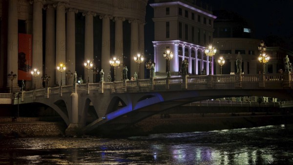 Illuminated bridge over a river at night with urban architecture in the background, Skopje, North Macedonia