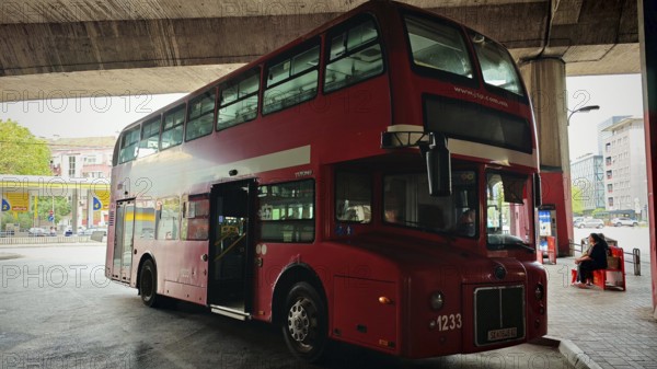 Classic red double-decker bus at a bus stop in an urban environment under a bridge, Skopje, North Macedonia