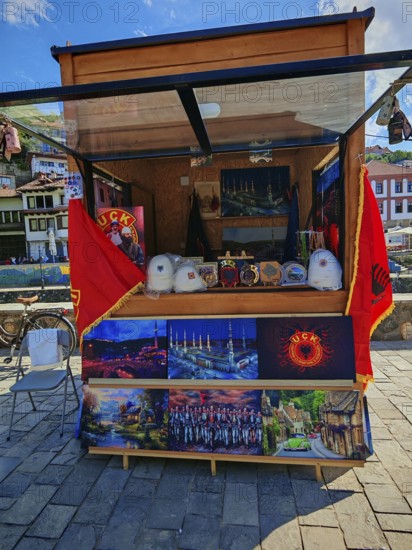 A sales stand with KLA souvenirs and flags under a blue sky, Prizren, Kosovo