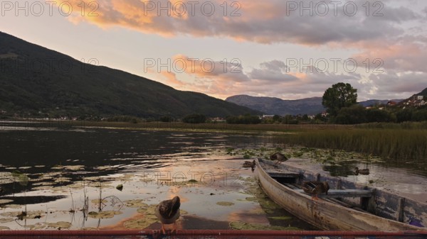 An old boat on a lake at sunset, with mountains and thick vegetation, Plav Lake, Montenegro