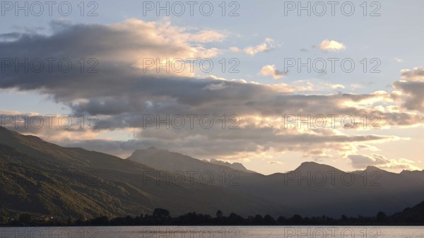 View of a mountain range with clouds glowing over a calm lake in the evening light, Plav Lake, Montenegro