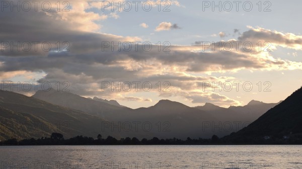 View across a lake to mountain silhouettes in warm sunset light, Plav Lake, Montenegro