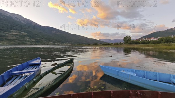 Three colorful boats on a calm lake at sunset surrounded by mountains and cloudy sky, Plav Lake, Montenegro