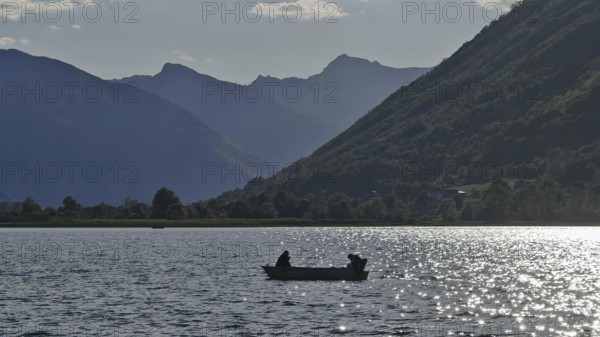 A boat with two people on a lake surrounded by mountain silhouettes in the evening light, Lake Plav, Montenegro