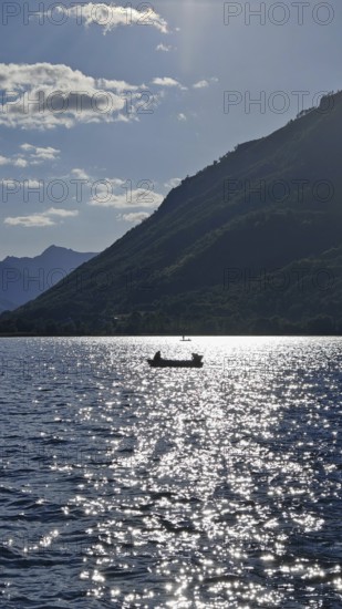 A lonely boat on a sparkling lake with mountains in the background and sunny atmosphere, Lake Plav, Montenegro