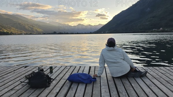 A person is relaxing on a jetty with a view of a quiet lake and mountains, Plav Lake, Montenegro