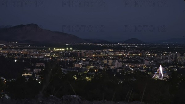 Nighttime city view with illuminated buildings, mountains in the background and dark sky, Podgorica, Montenegro