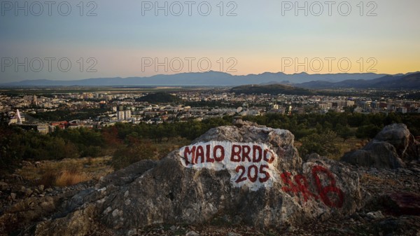 Panoramic view of a city in evening light with surrounding mountains and painted rock in the foreground, Podgorica, Montenegro