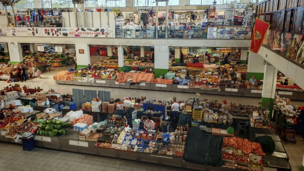Large market hall with numerous stands and products. People buy fresh food. Lively atmosphere, Ulcinj, Montenegro