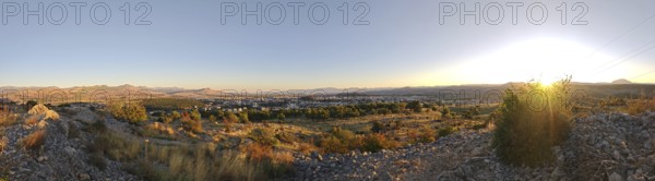 A city surrounded by nature with trees in the foreground and mountains in the background, illuminated by a warm sunset, looking out from a hill on the outskirts of Podgorica, Montenegro
