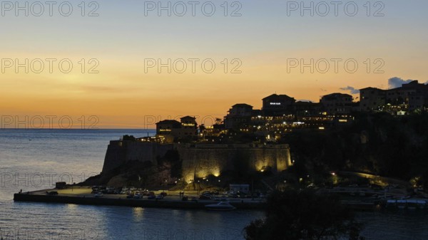 Dusk over an illuminated fortress on a coast with calm sea and warm sky, Ulcinj, Montenegro