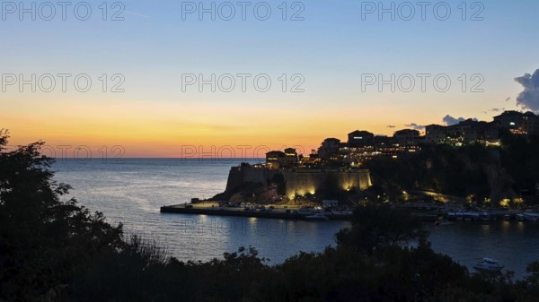 Sunset over a coastal town with silhouetted buildings and a calm sparkling sea, Ulcinj, Montenegro