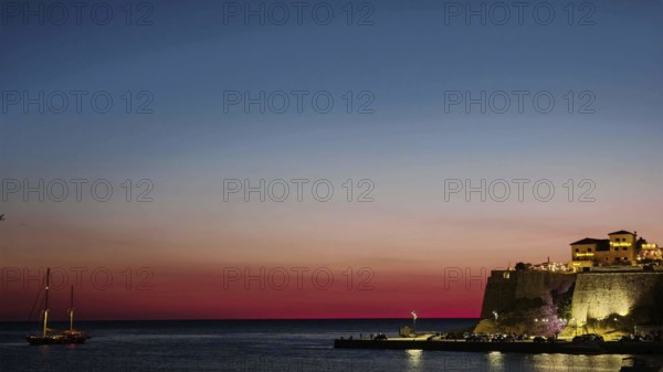 A sailboat sails under a colorful sky at sunset on calm sea, Ulcinj, Montenegro