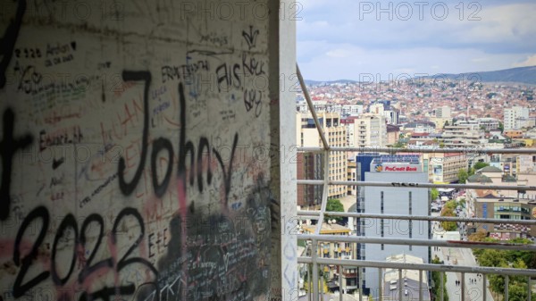 A graffiti-covered building offers a view of an urban landscape under a cloudy sky, Pristina, Kosovo