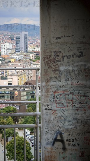 Wall with graffiti in the foreground, urban buildings and skyscrapers in the background, Pristina, Kosovo